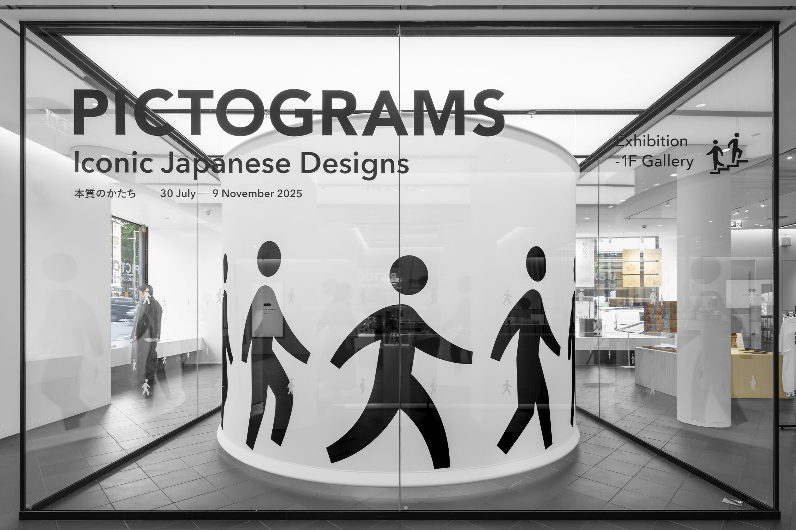 View from outside the exhibition hall revealing the main display of Japanese pictogram designs through the glass facade.