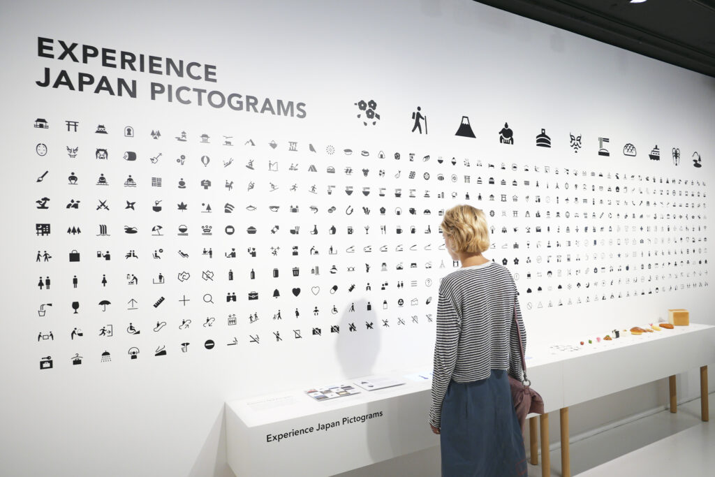 Visitors observing a wall of pictograms designed for the Pictograms exhibition.